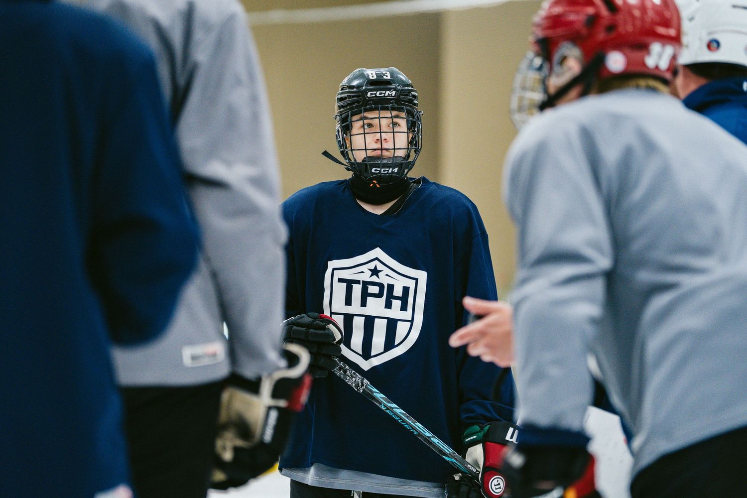 Young hockey player in TPH jersey listens attentively during an ice hockey training session.