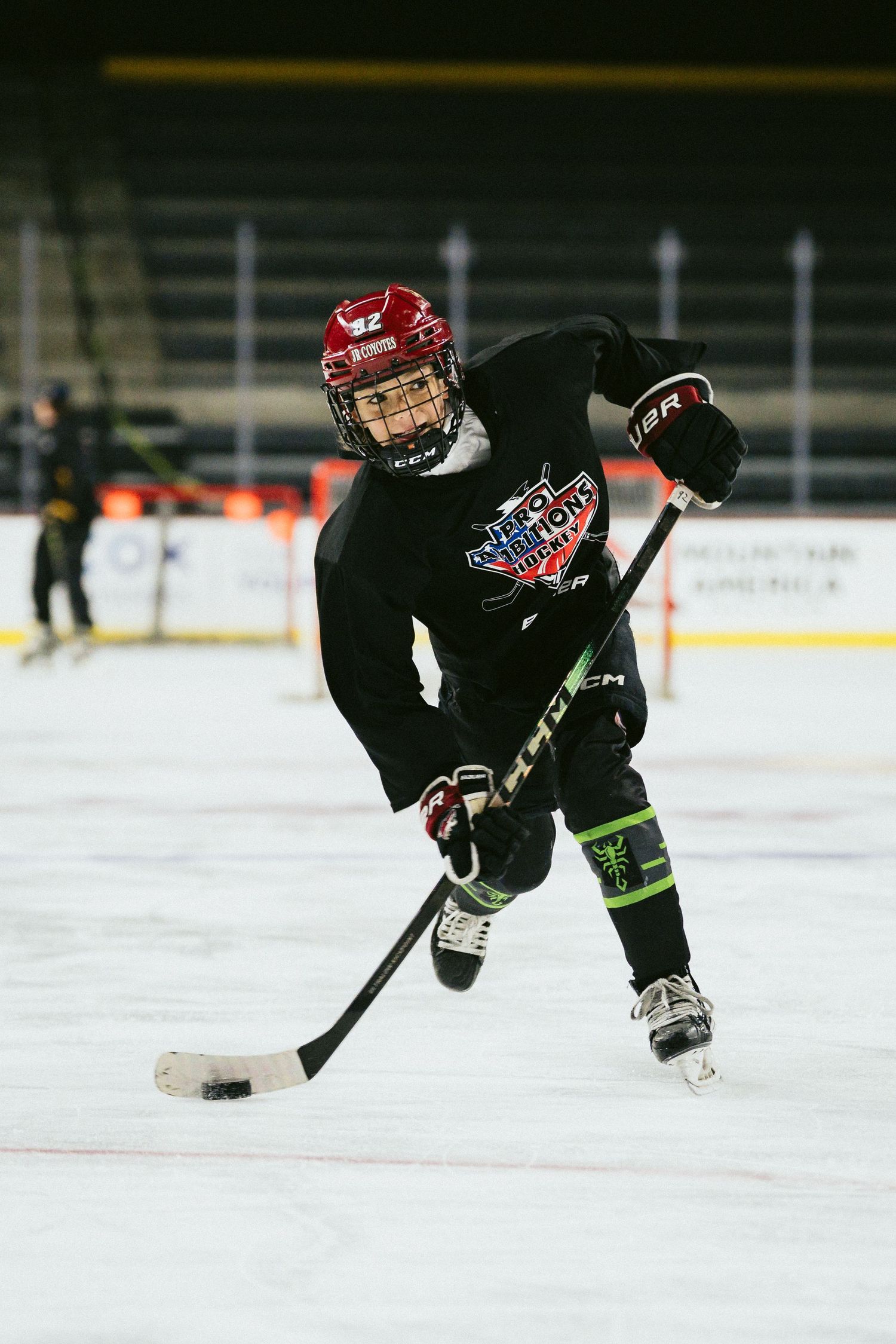 Youth hockey player in black jersey and red helmet handling puck on indoor ice rink.