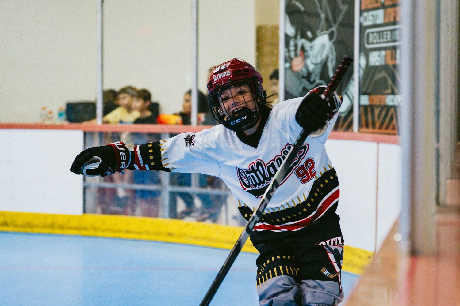 Young ice hockey player in white uniform celebrating on rink, holding stick with arms raised in victory.