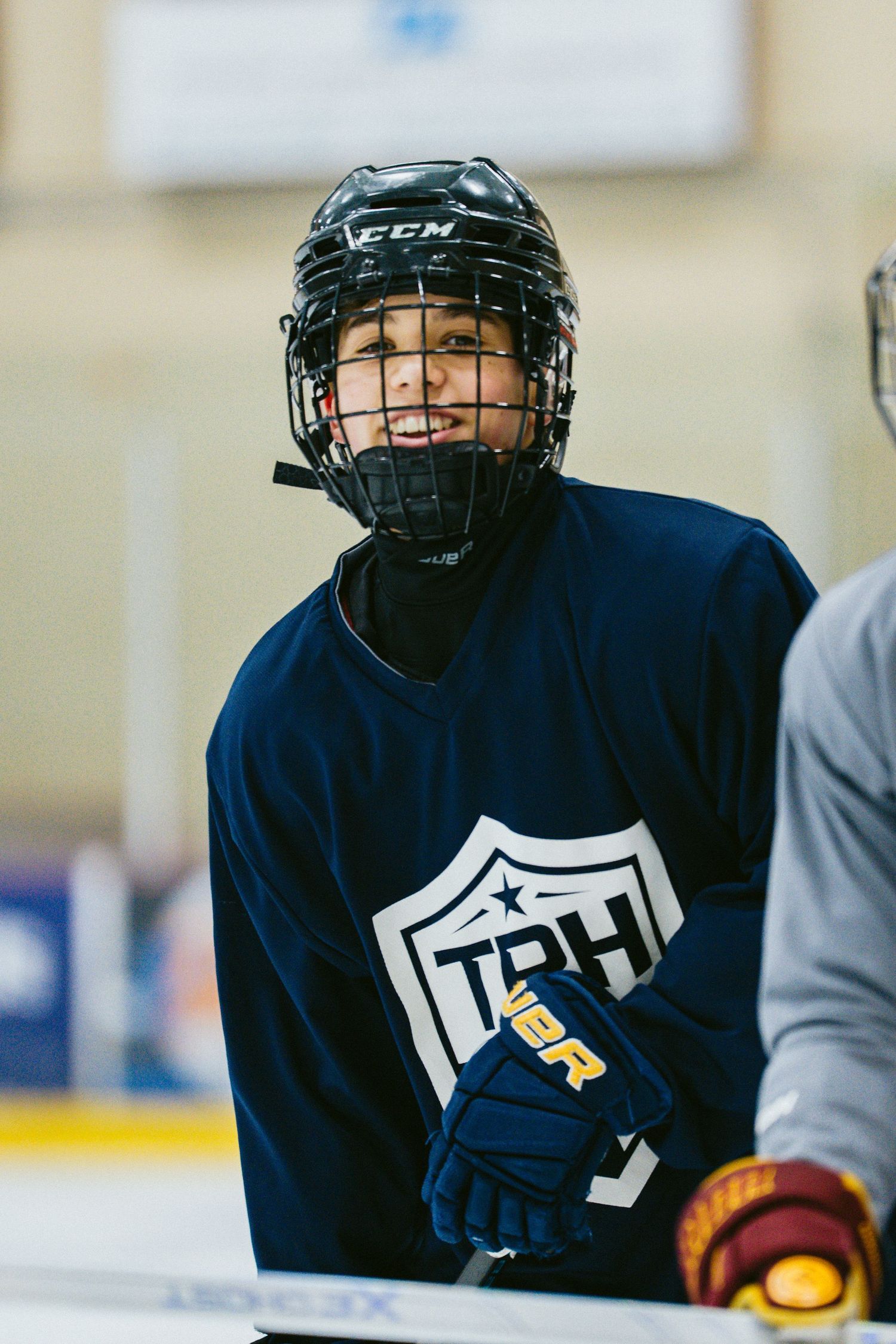 Young hockey player in a navy TPH jersey and black CCM helmet looks up attentively during ice hockey practice.