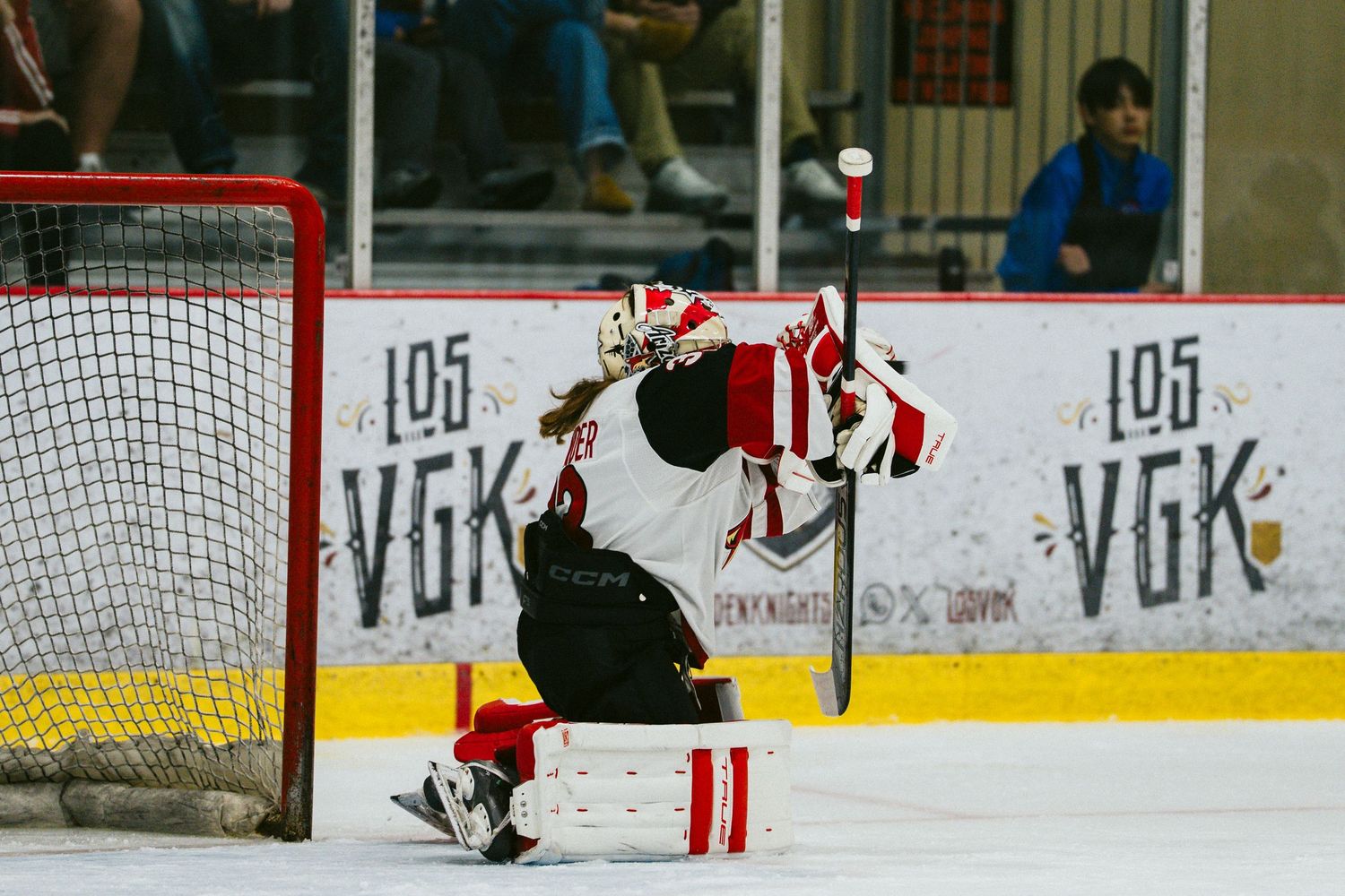 Hockey players in red and white jerseys position themselves near the goal during gameplay.