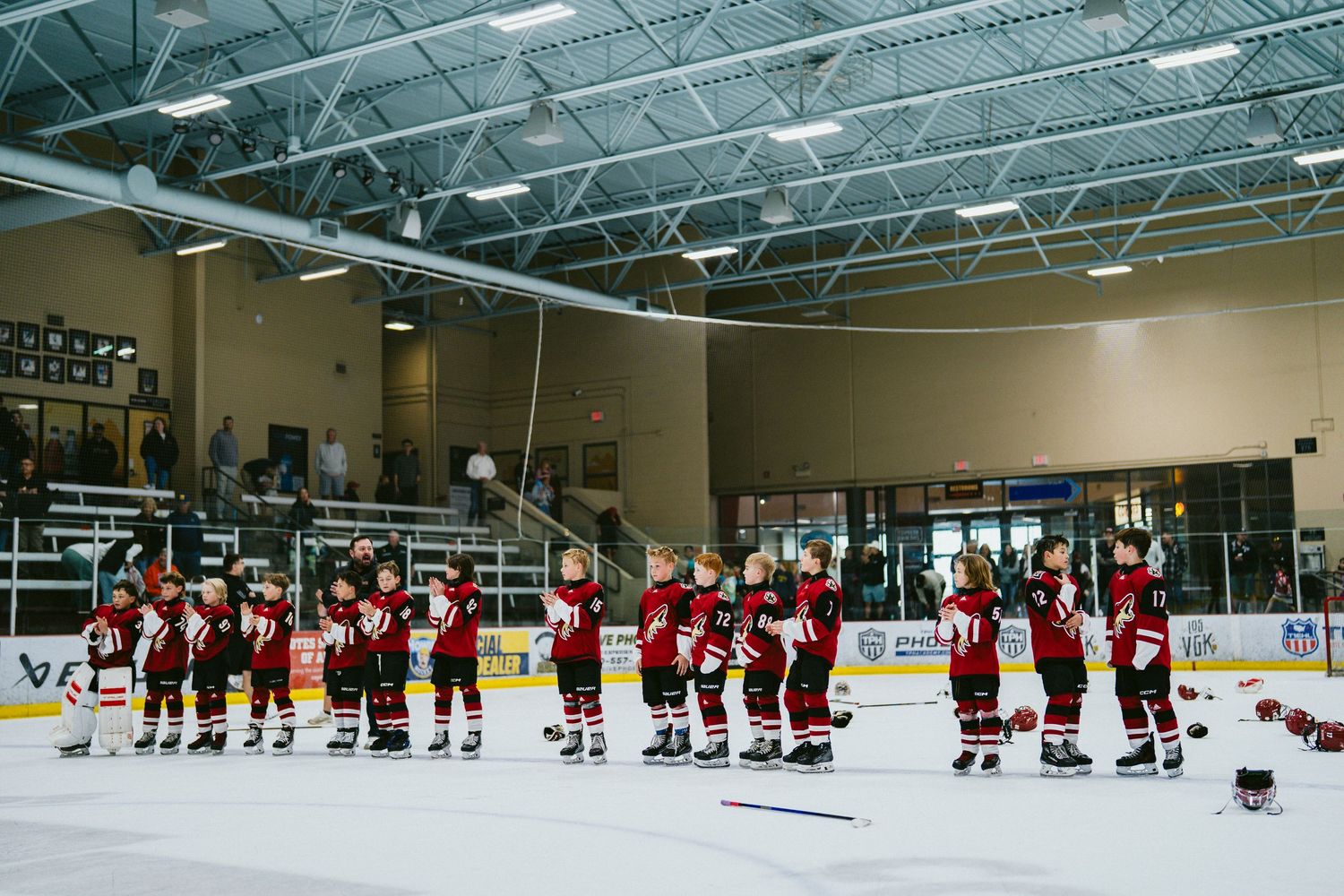 Youth hockey team in red uniforms lined up along the boards during a game.