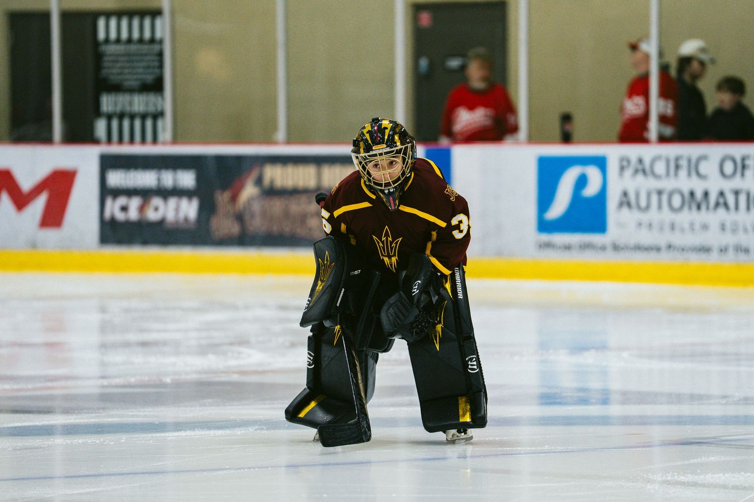 Hockey players in black and red uniforms compete for the puck on an ice rink with advertising boards visible.