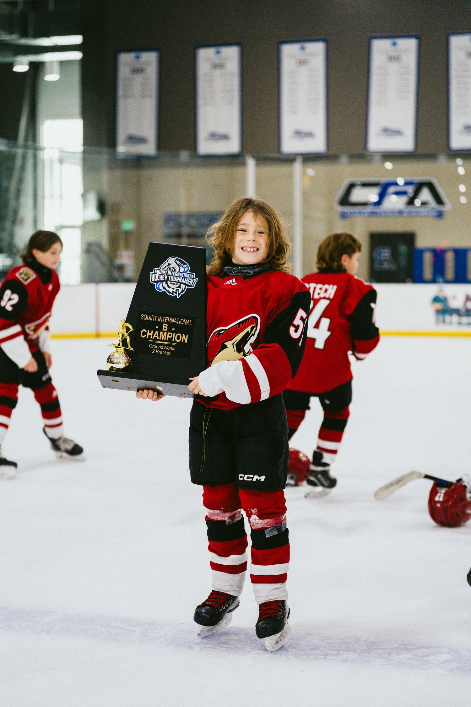 Youth hockey players in red jerseys skating with awards on indoor ice rink.