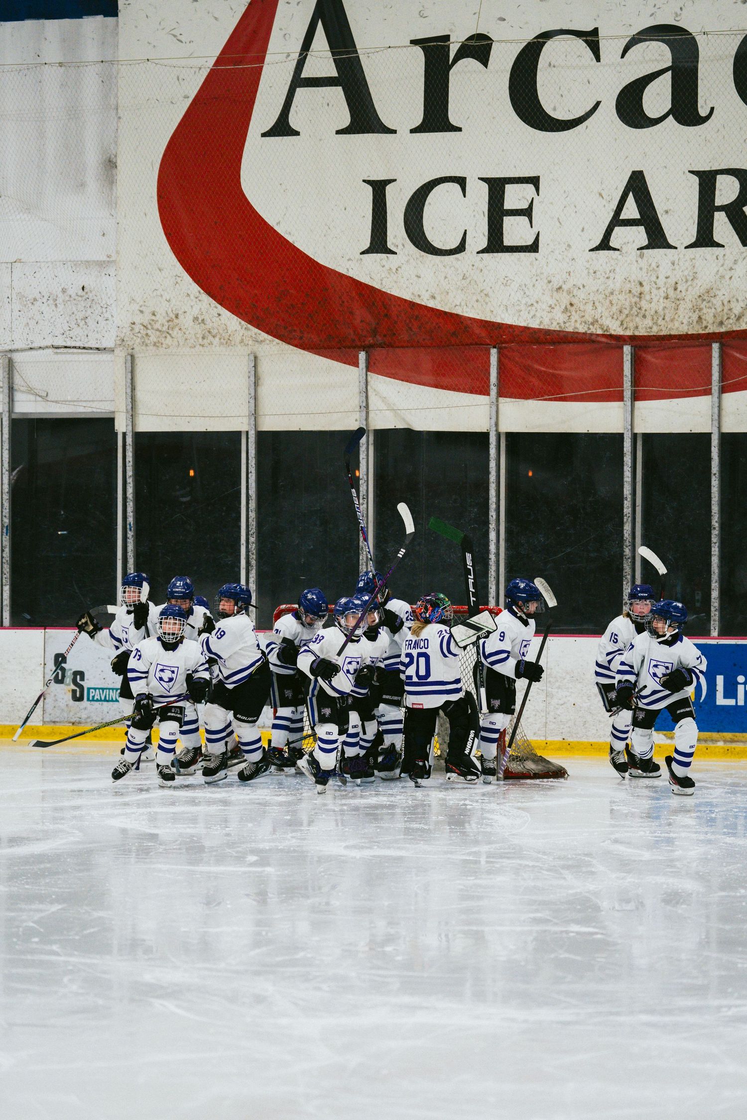 Youth hockey team in blue and white uniforms stretches together on the ice rink.