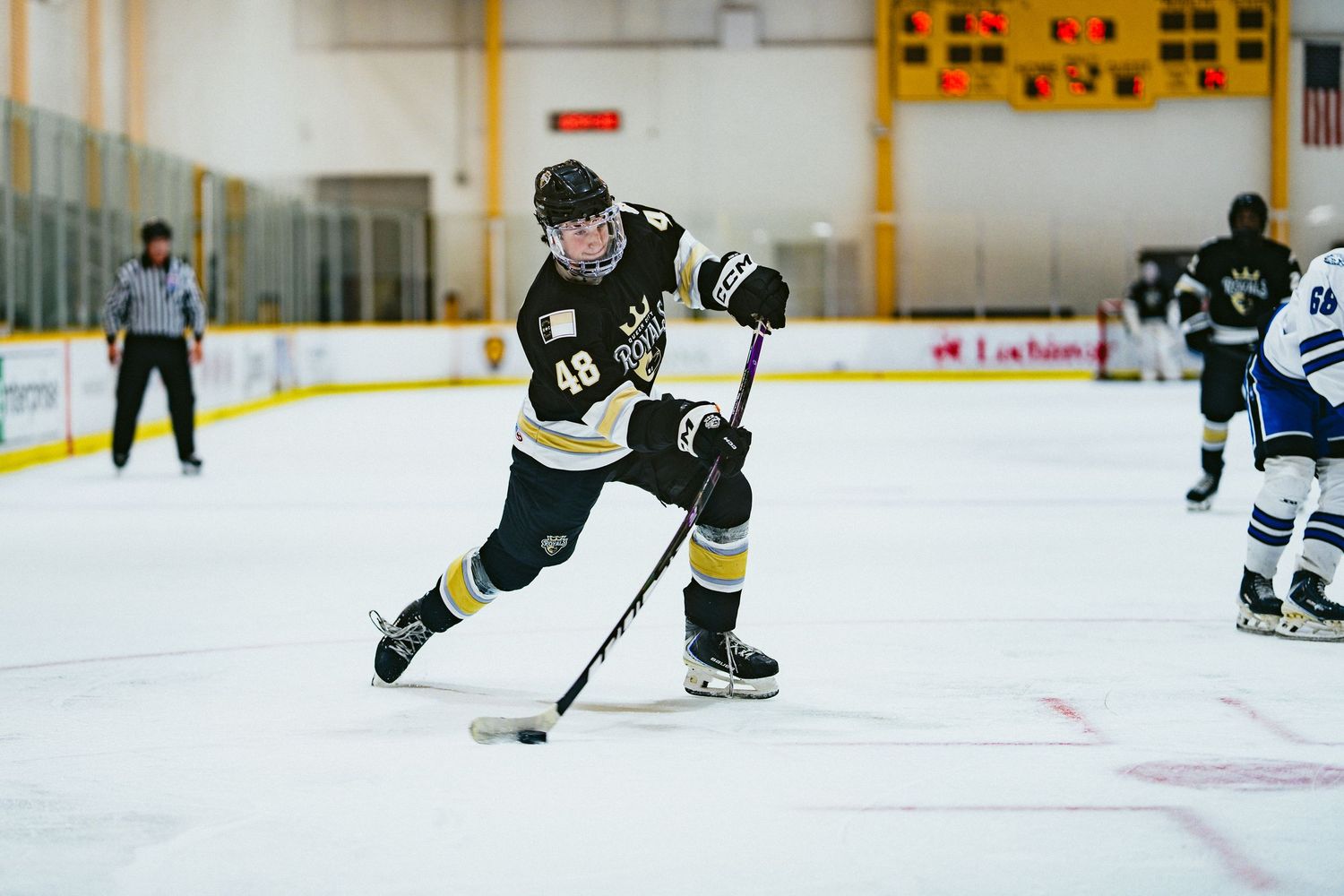 Hockey player number 48 in black and gold uniform handles the puck on indoor ice during a competitive game.