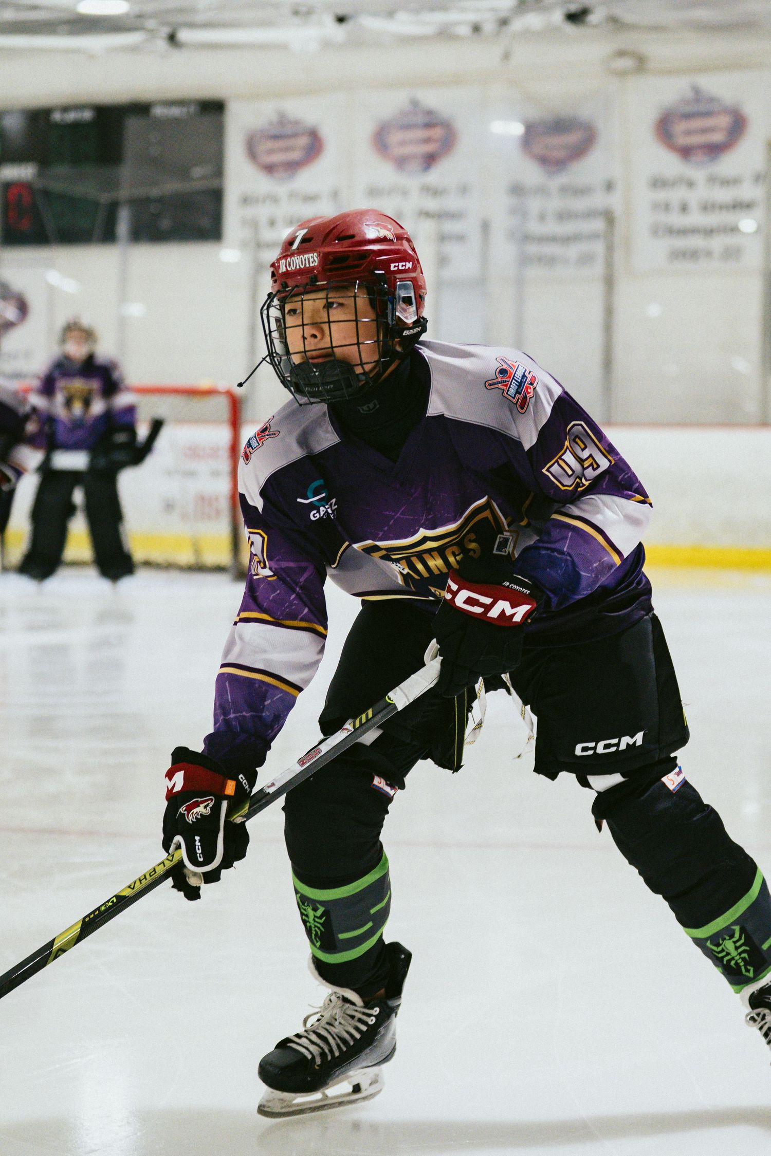 Young hockey player in purple CCM jersey ready for play during a youth ice hockey game.