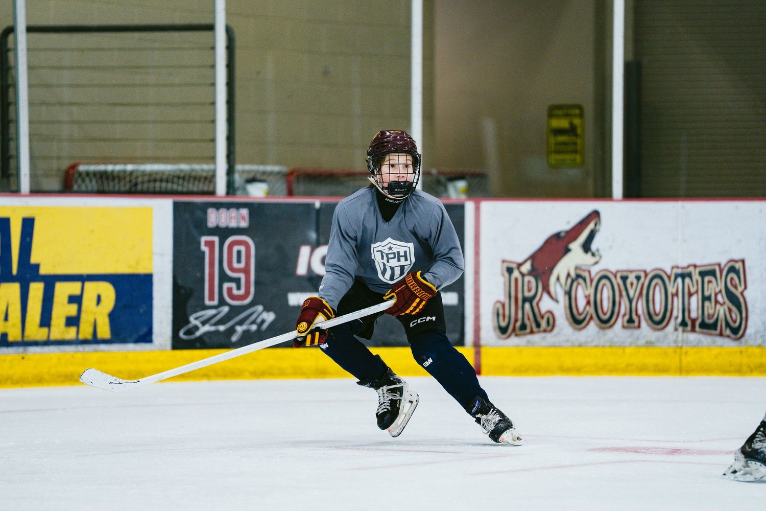 Young hockey player skates with stick during practice at Jr. Coyotes indoor ice rink.