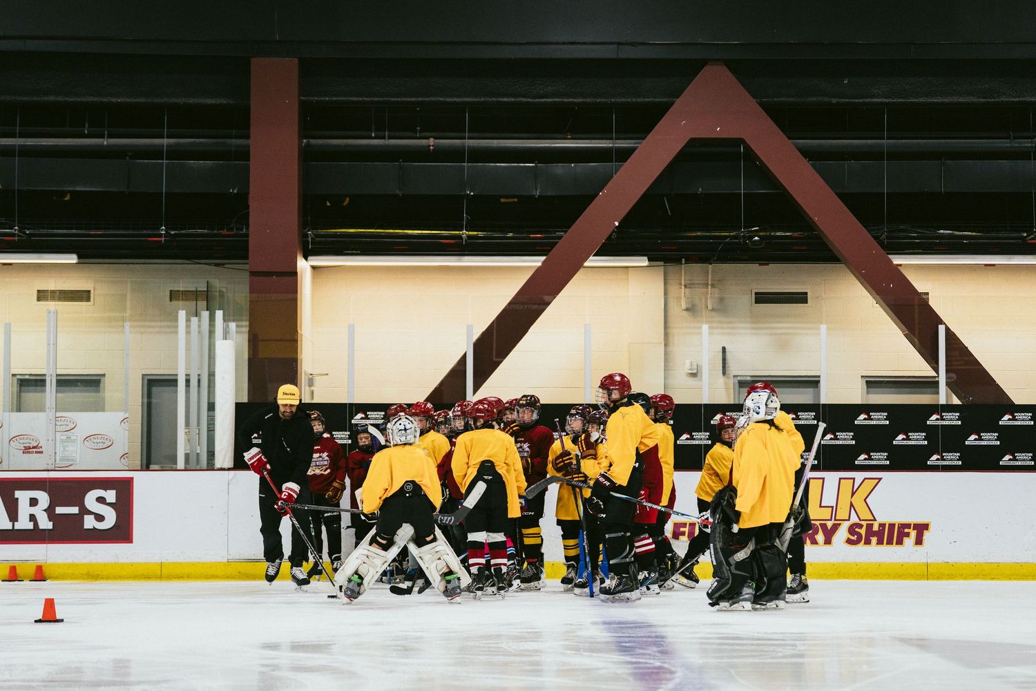 Youth hockey team huddles together on ice rink during practice session indoors.