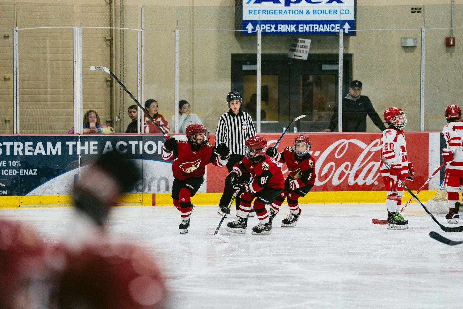 Youth hockey players in red and black jerseys skating on ice during a game or practice session.