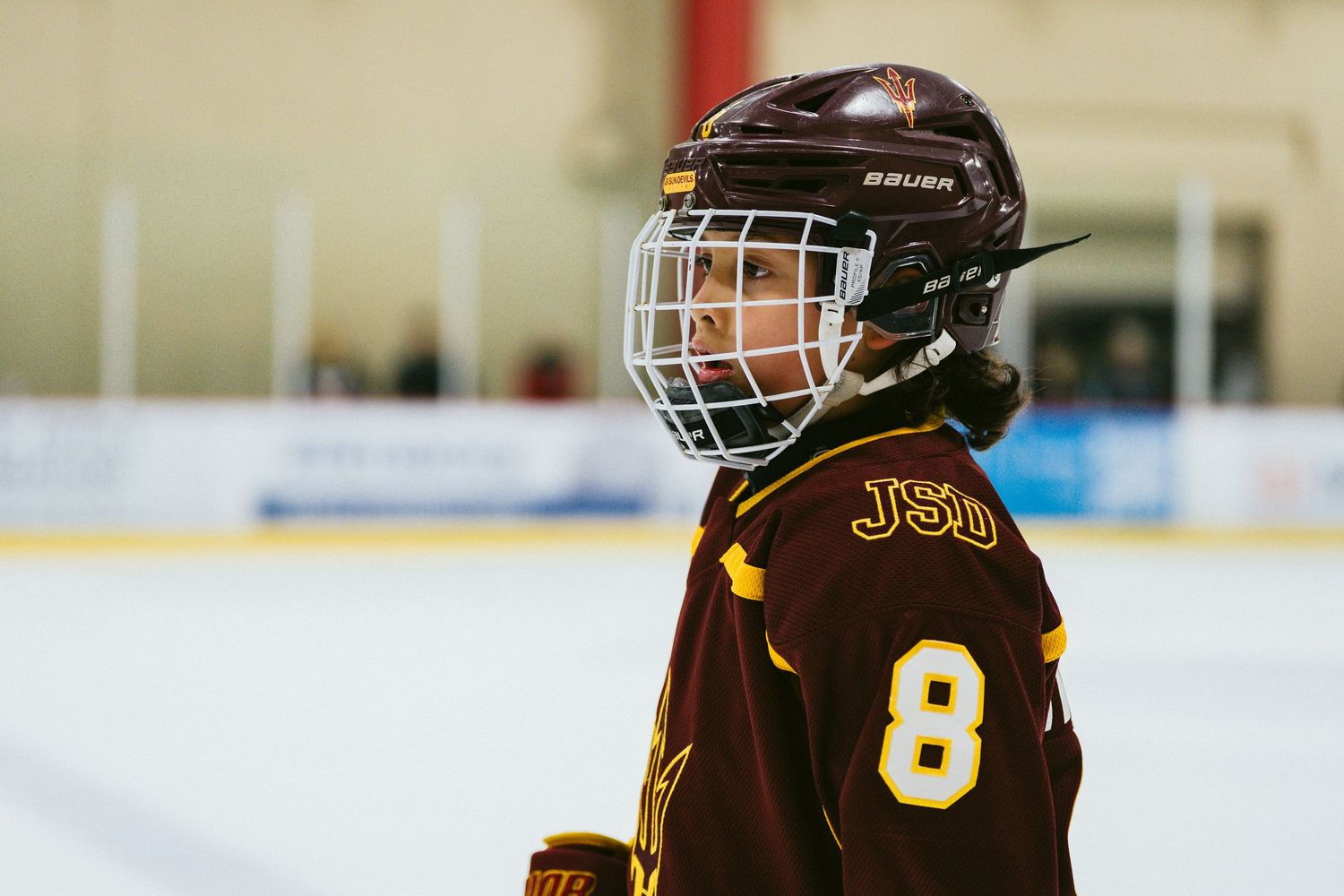 Youth hockey players in brown uniforms with gold trim skate during a game.