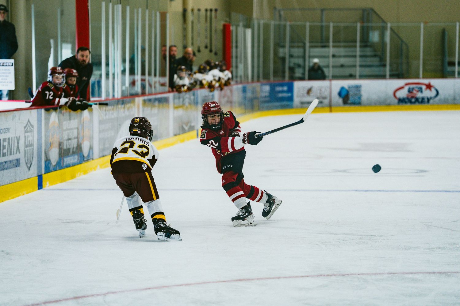 Two youth hockey players battle for control of the puck during a competitive match on the ice.