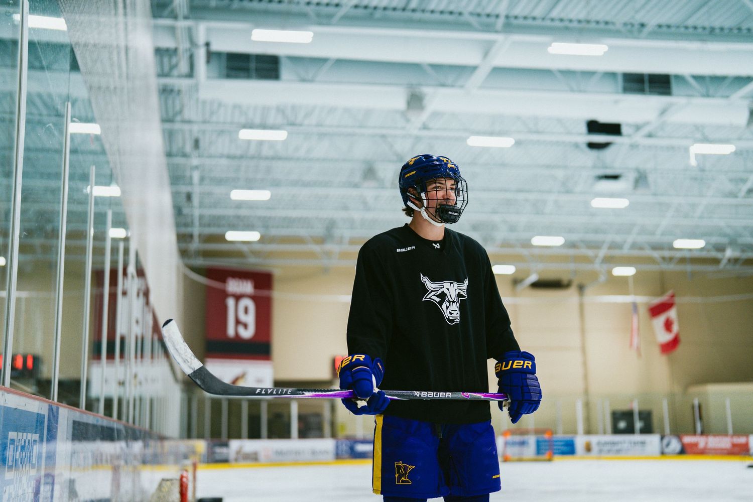 Hockey player in black jersey holding a stick on an indoor ice rink, wearing a helmet with visor.