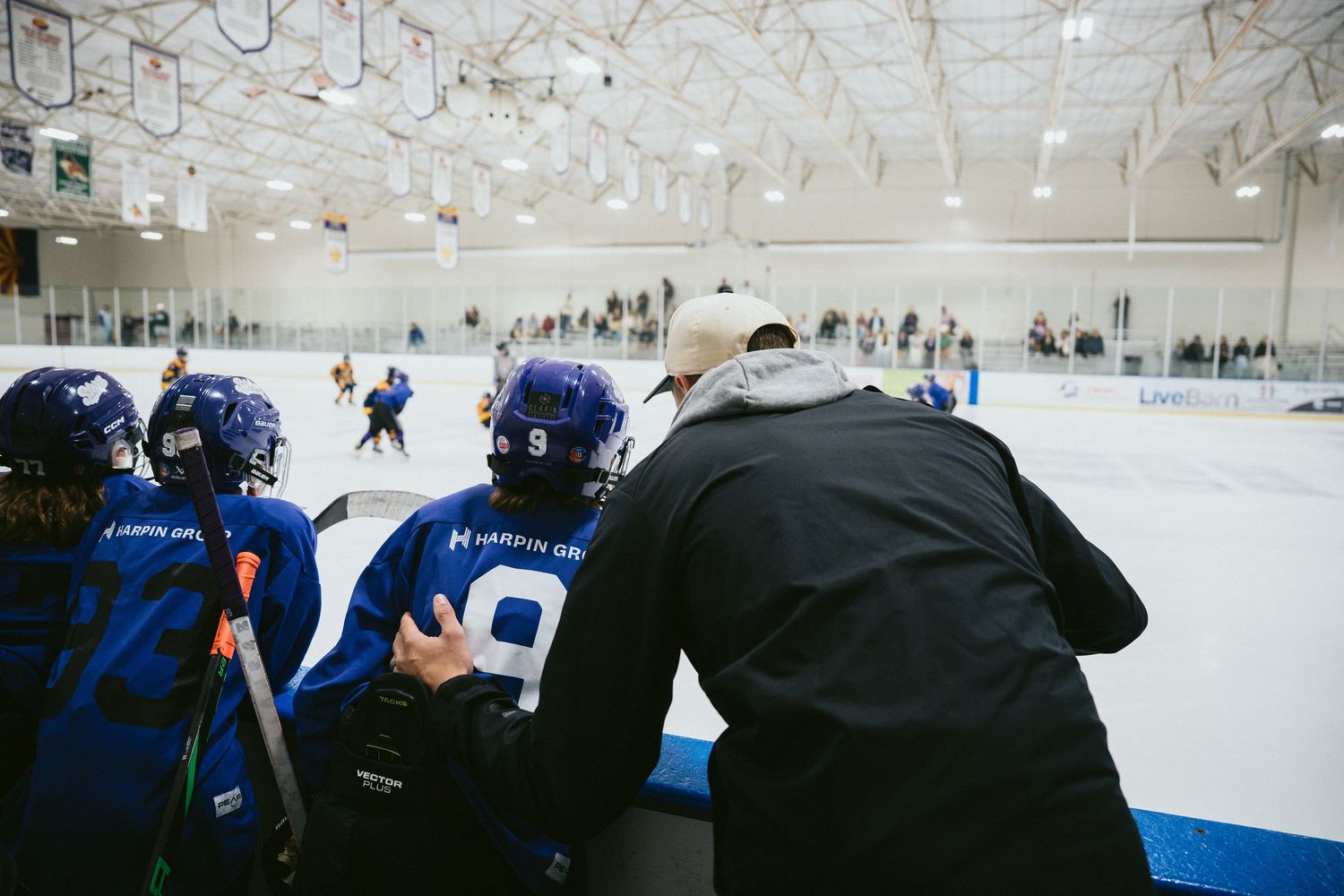 Hockey coach instructs young players in blue jerseys at the bench during youth ice hockey game.