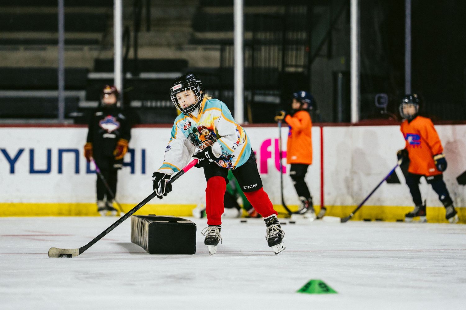 Young girl hockey player practices puck handling with cone drills during indoor ice hockey training.