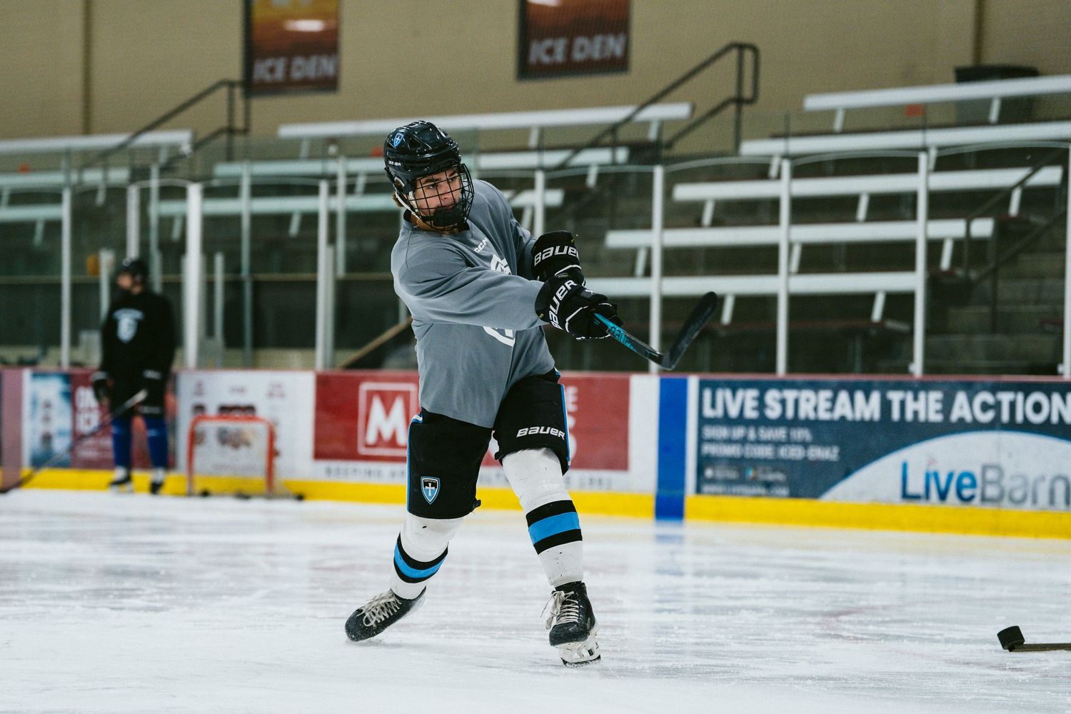 Hockey player taking a powerful shot on ice during game at Ice Den arena.