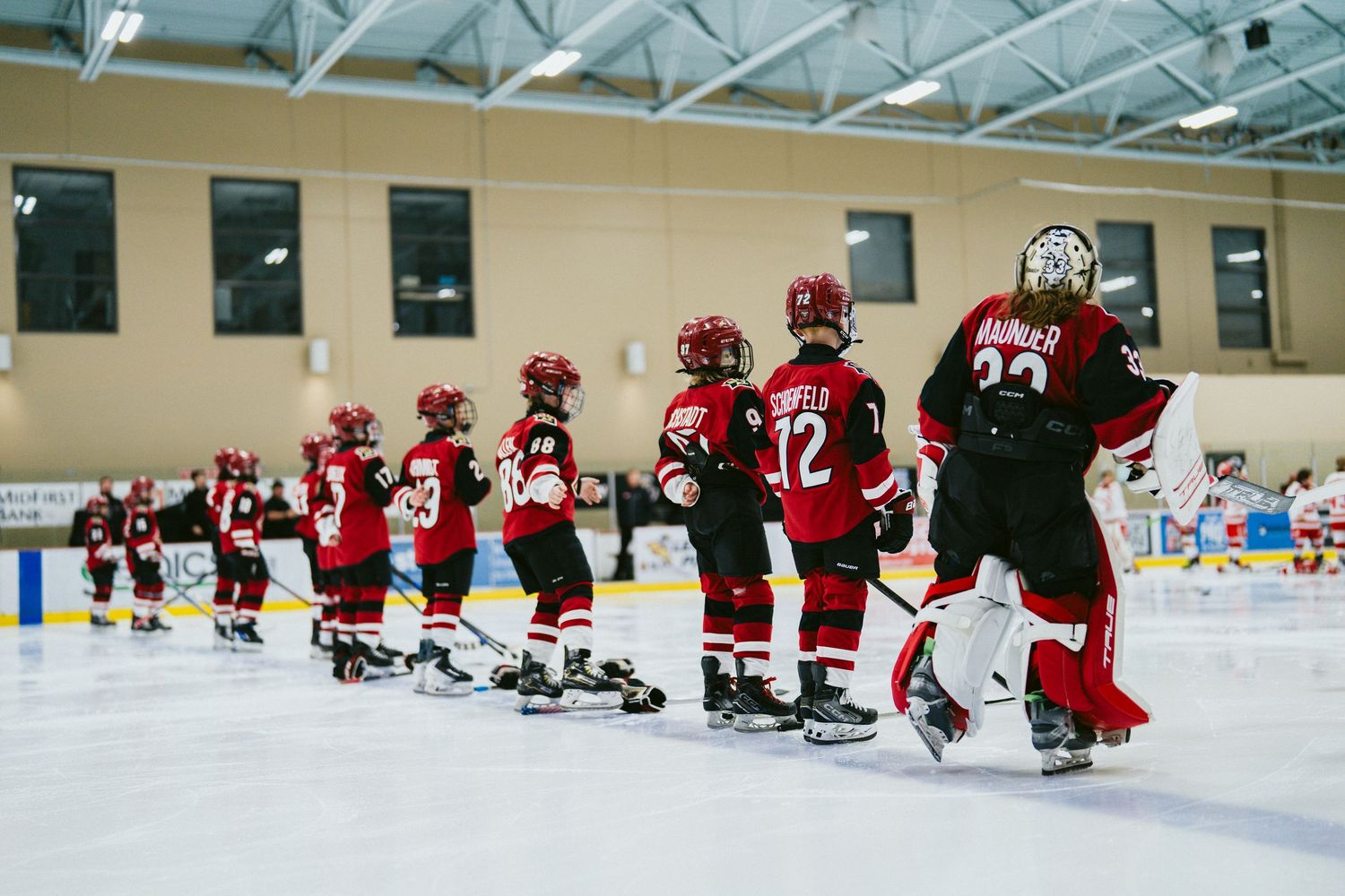 Wide view of hockey players lined up along the boards during practice at an indoor ice arena.