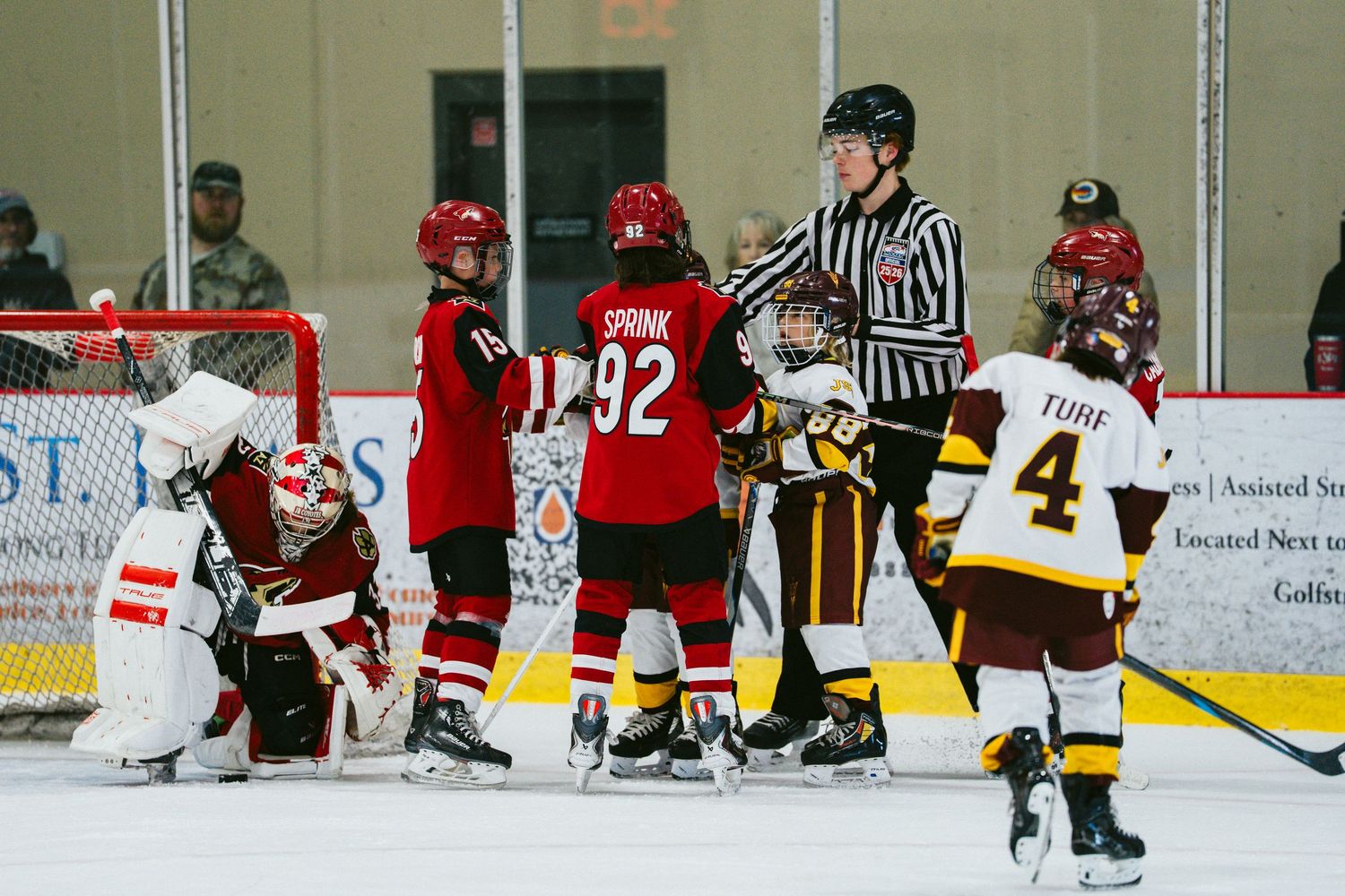 Wide shot of youth hockey game showing multiple players from both teams spread across the ice rink.