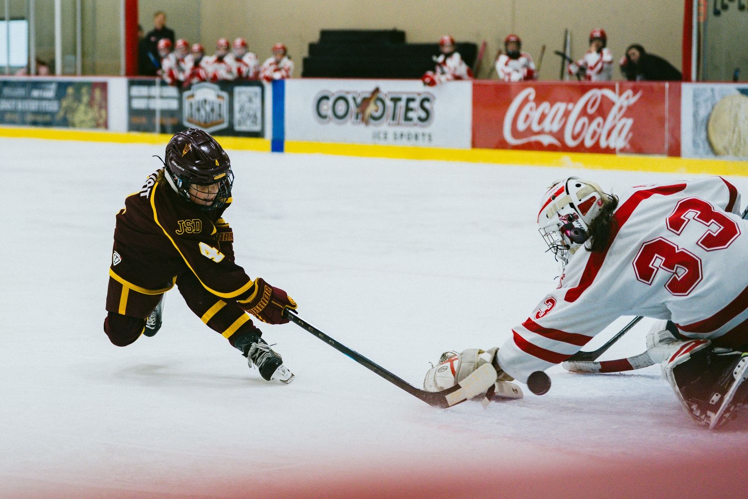 Hockey players battle for the puck during an intense game with a Coyotes logo visible in the background.