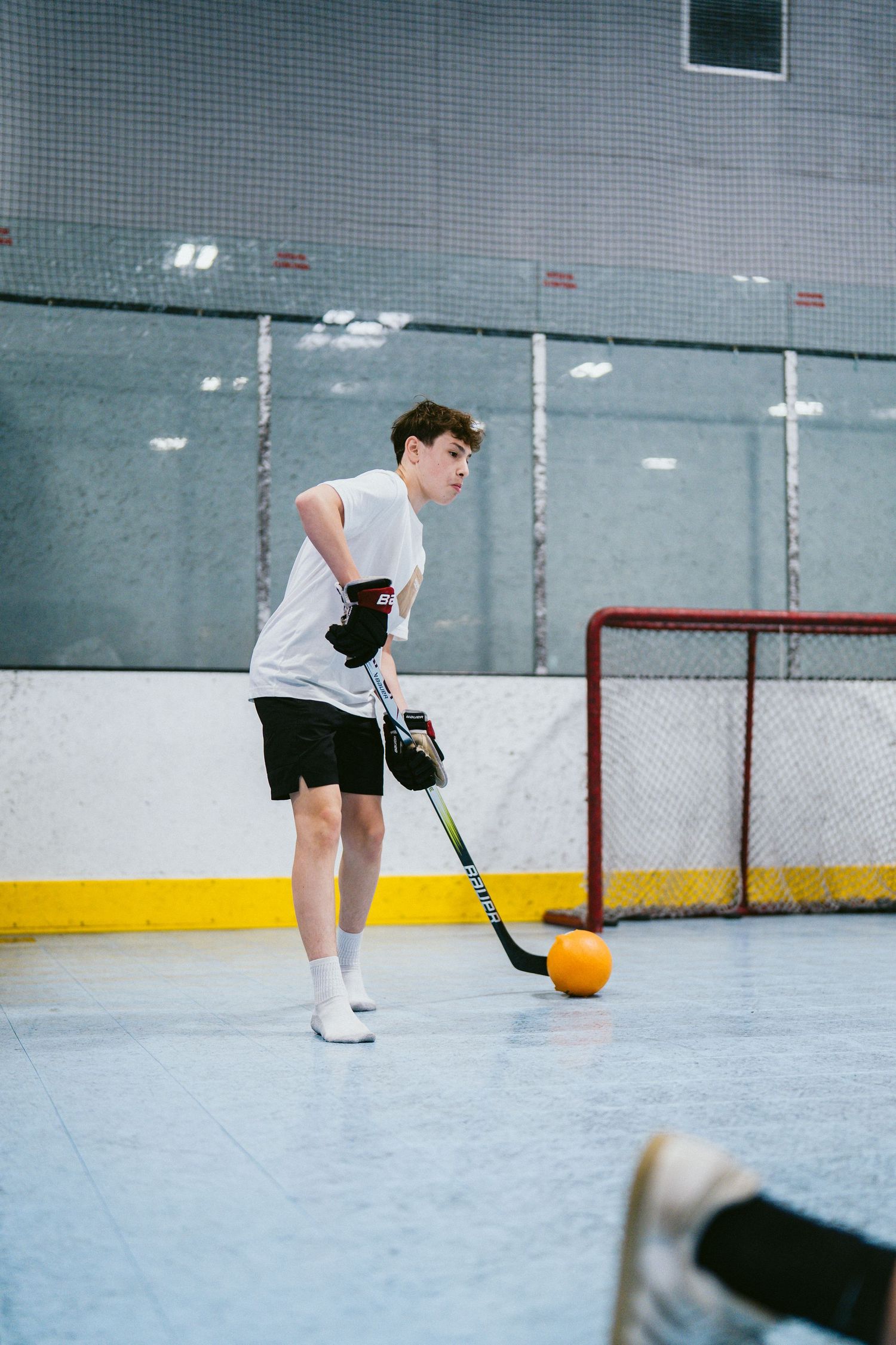 Teen hockey player practicing stickhandling with an orange ball on an indoor rink near a red goal net.