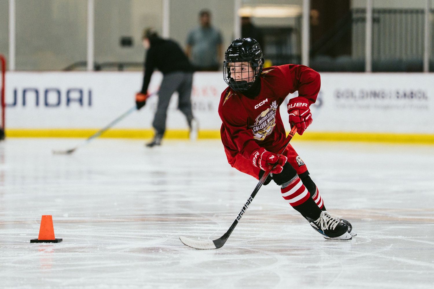 Young hockey player in red uniform skating with stick during ice hockey practice drill.