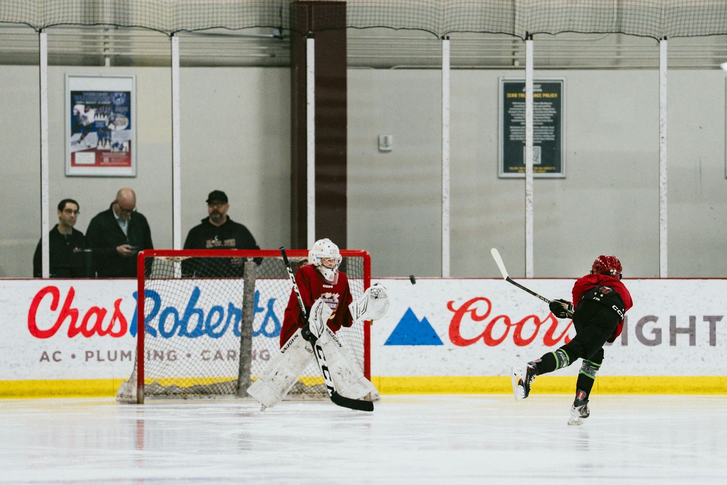 Hockey goalie defends the net as a player shoots during indoor ice rink practice session.