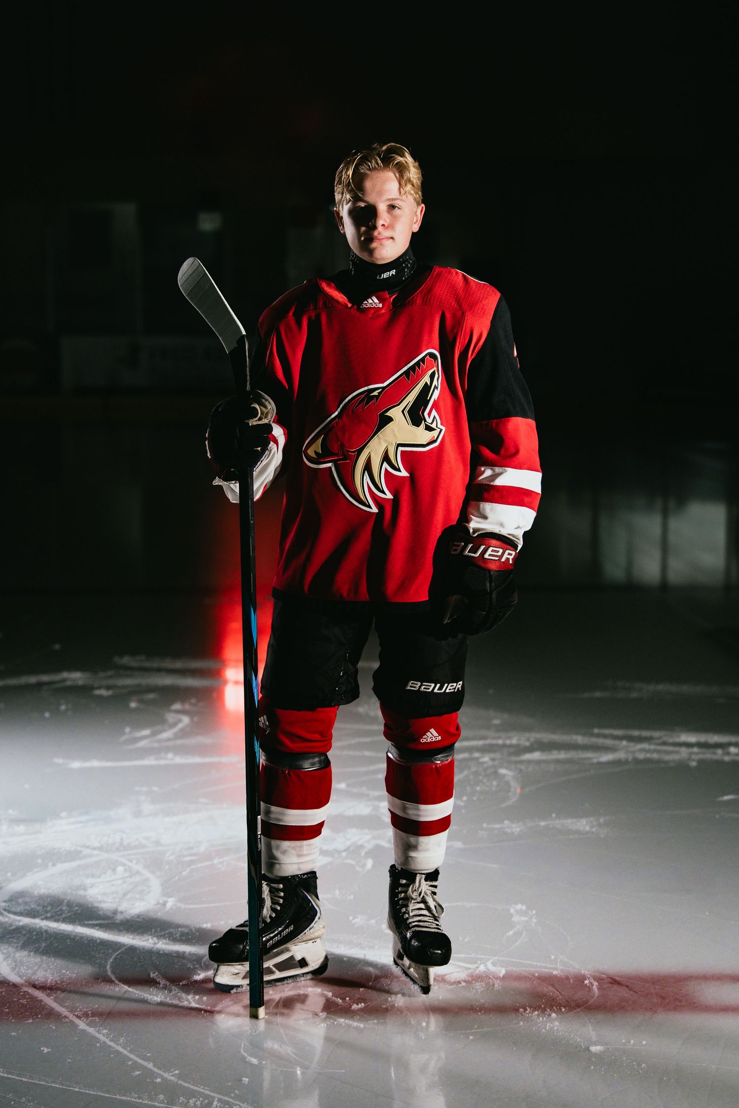 Hockey player in red Arizona Coyotes jersey holding a stick on ice in dramatic dark lighting.