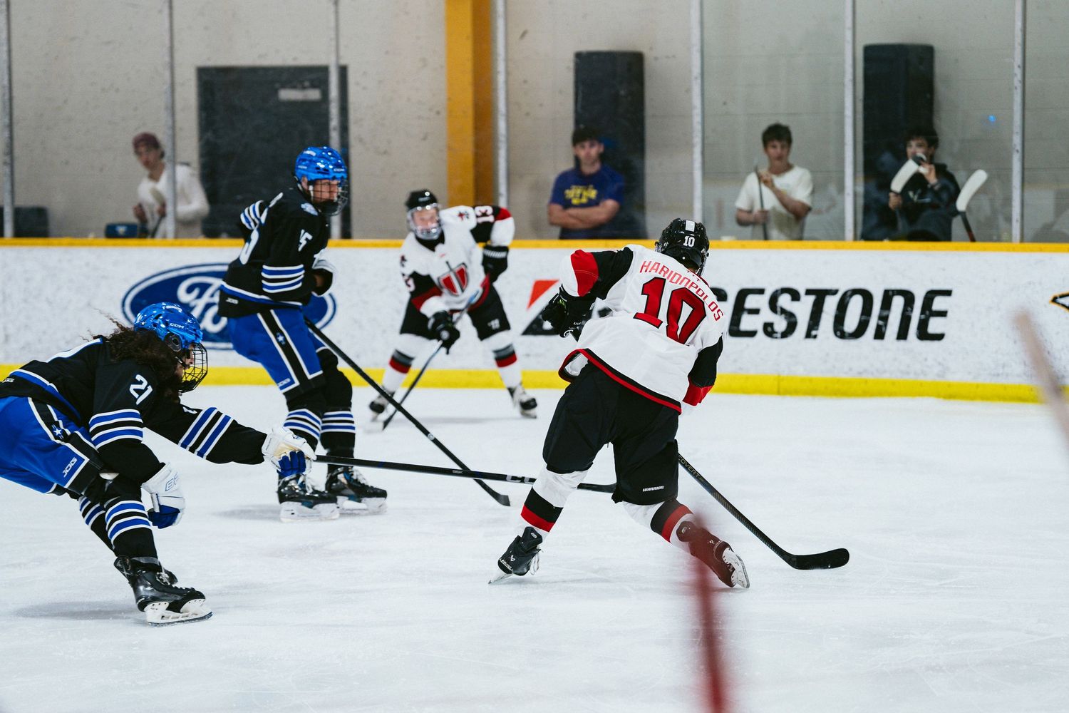Hockey player number 10 in red and white takes shot on ice against blue and white defenders.