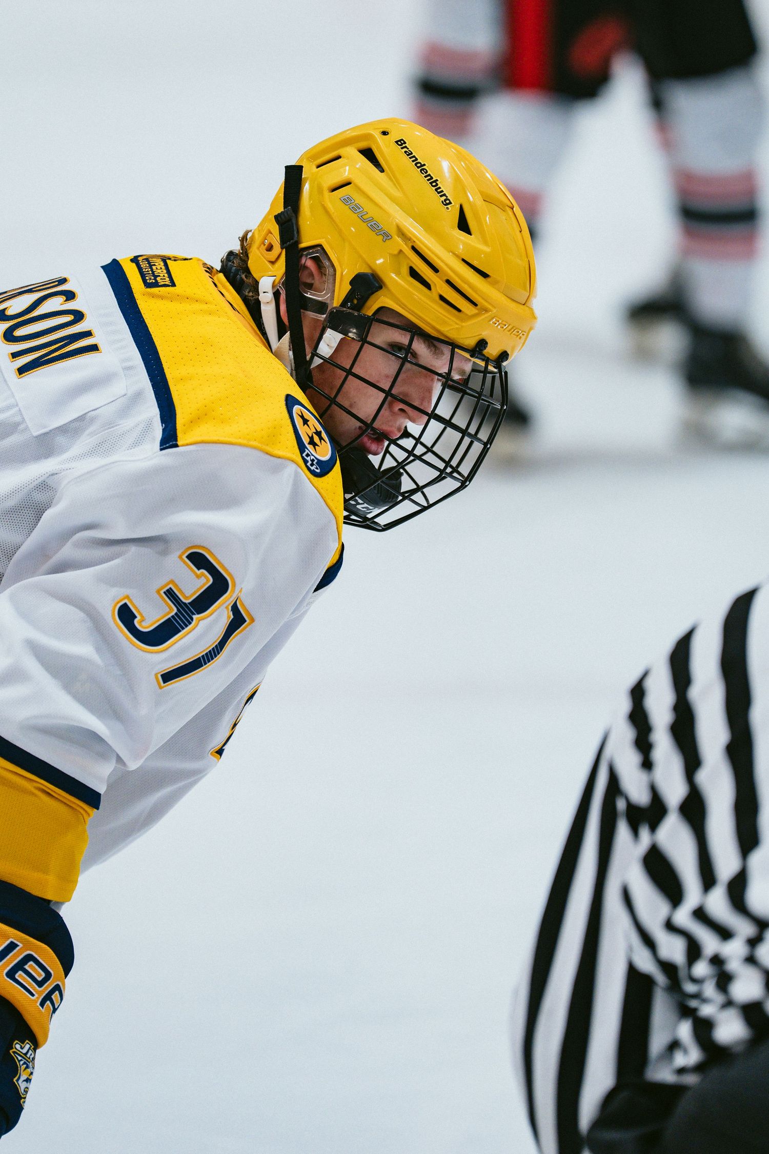 Ice hockey player number 31 in yellow helmet focuses intently at a face-off near a referee.