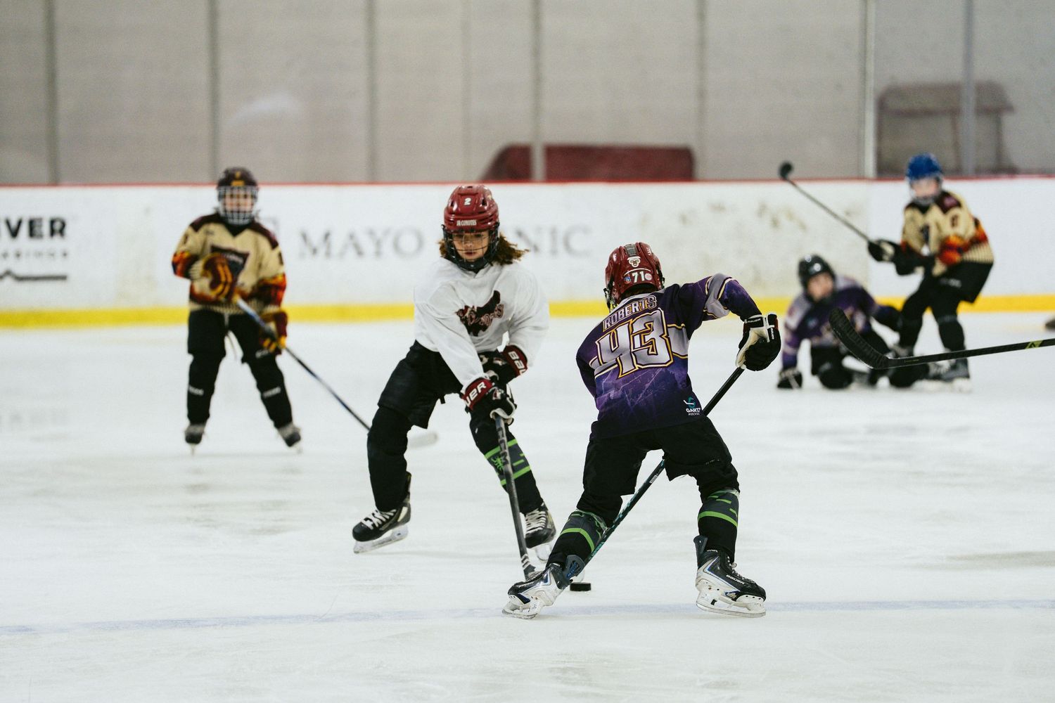 Youth hockey players compete for puck control during a fast-paced ice hockey game.