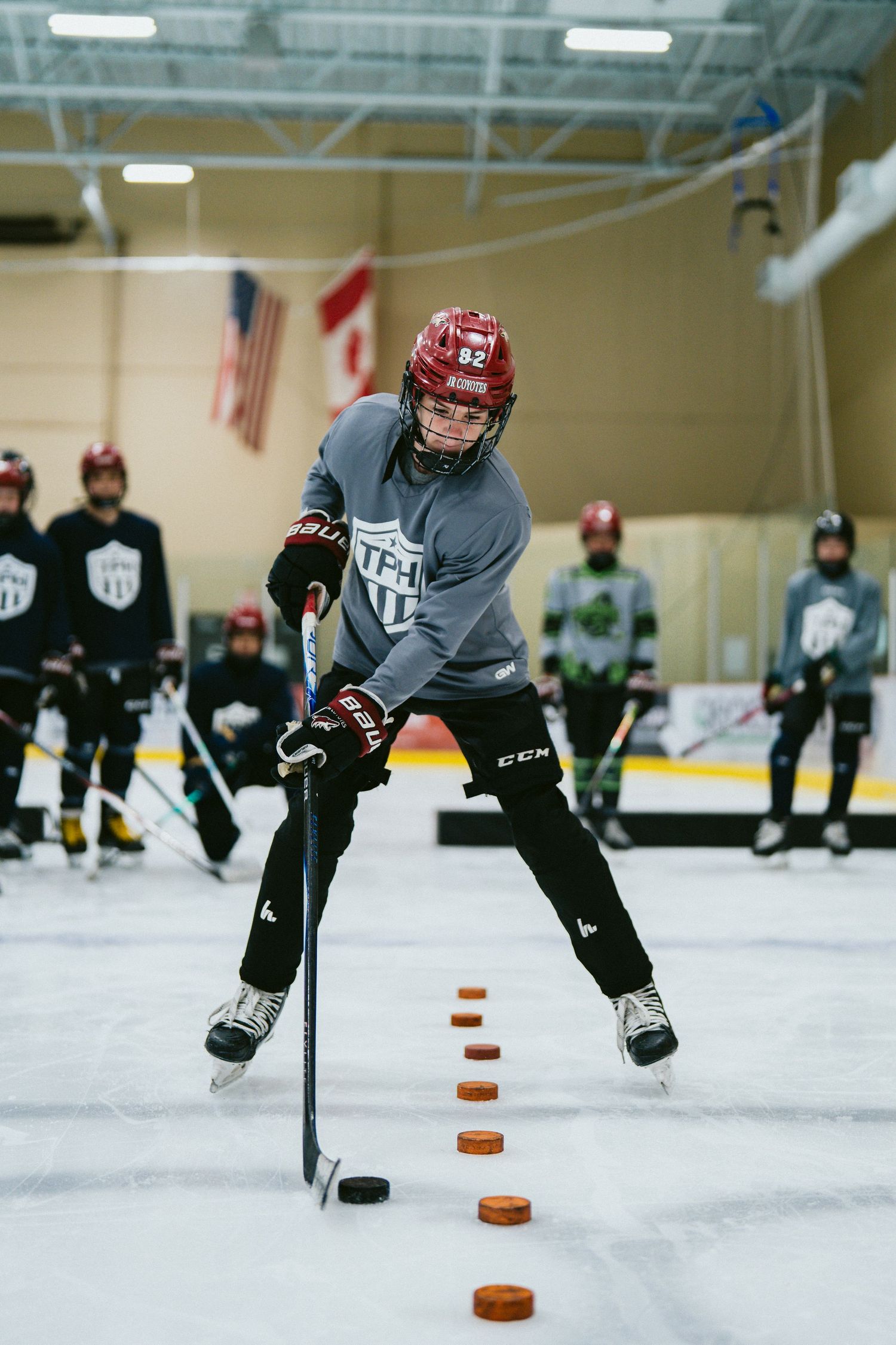 Young hockey player practicing stickhandling drills with pucks on an indoor rink during a CCM hockey training camp.