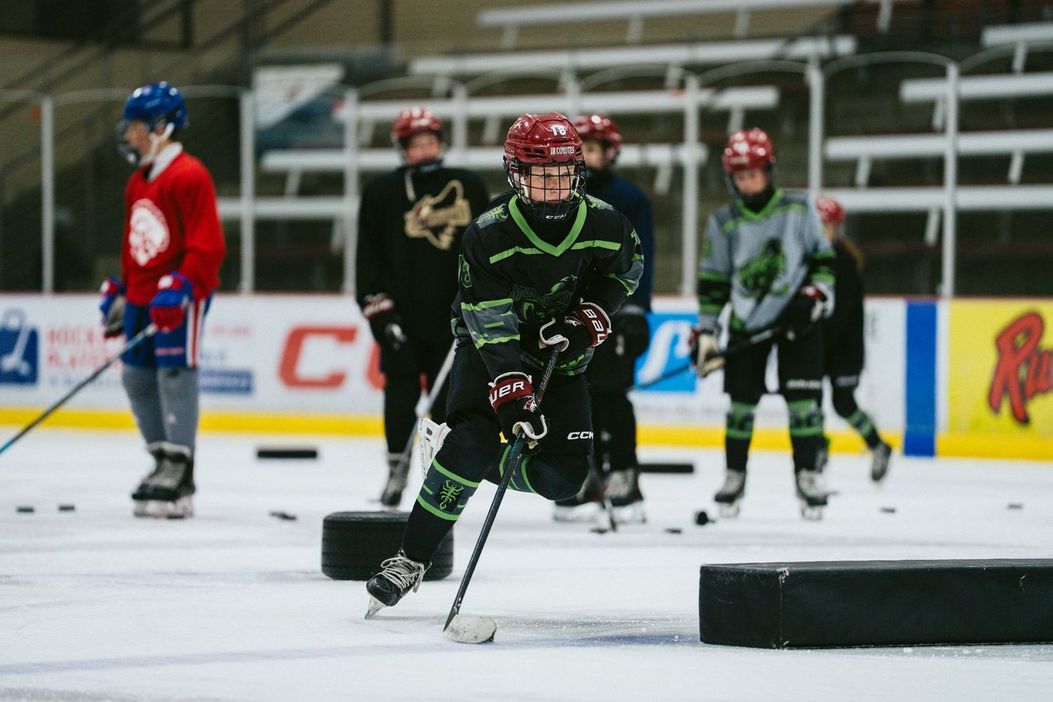 Youth hockey player in black and green jersey skates with a puck during indoor ice hockey practice.