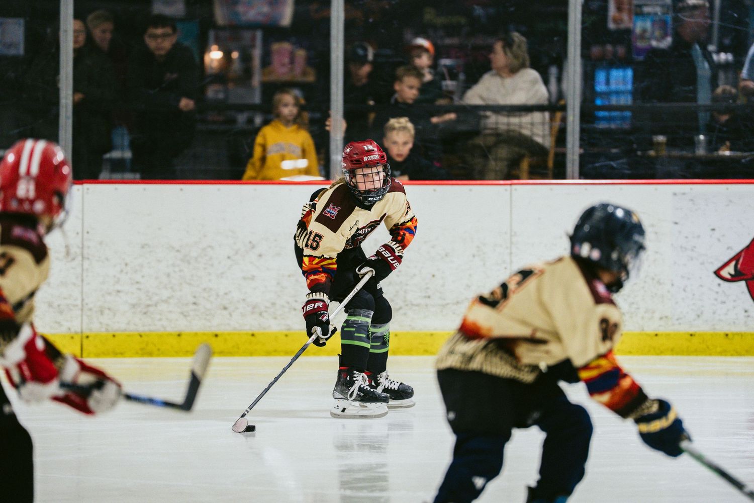 Young hockey player controls the puck on ice during a youth hockey game with spectators watching.
