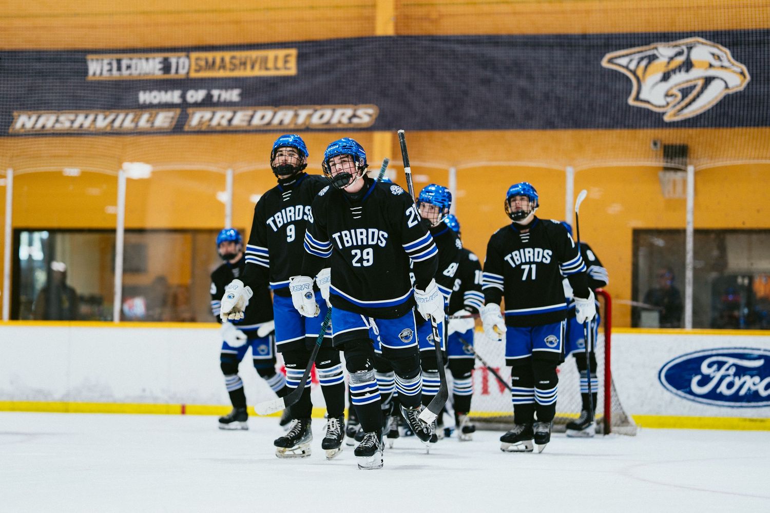 Hockey players in black Tribs uniforms skate onto the ice beneath a Nashville Predators welcome banner.