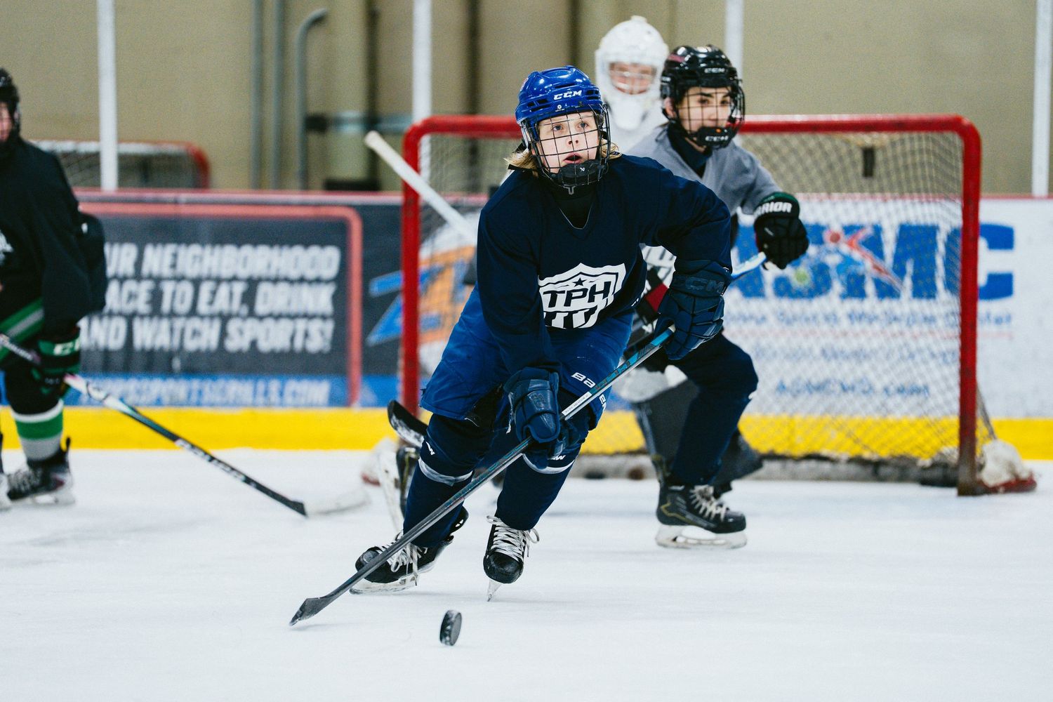Female hockey player in blue TPH jersey skates with puck during indoor ice rink practice session.