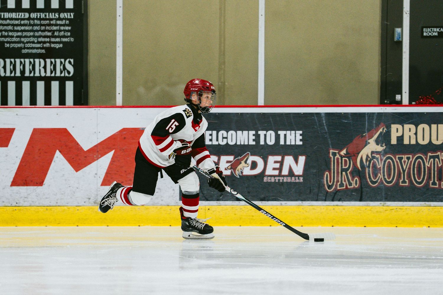 A hockey player skates on ice near the rink boards with advertisements visible in the background.