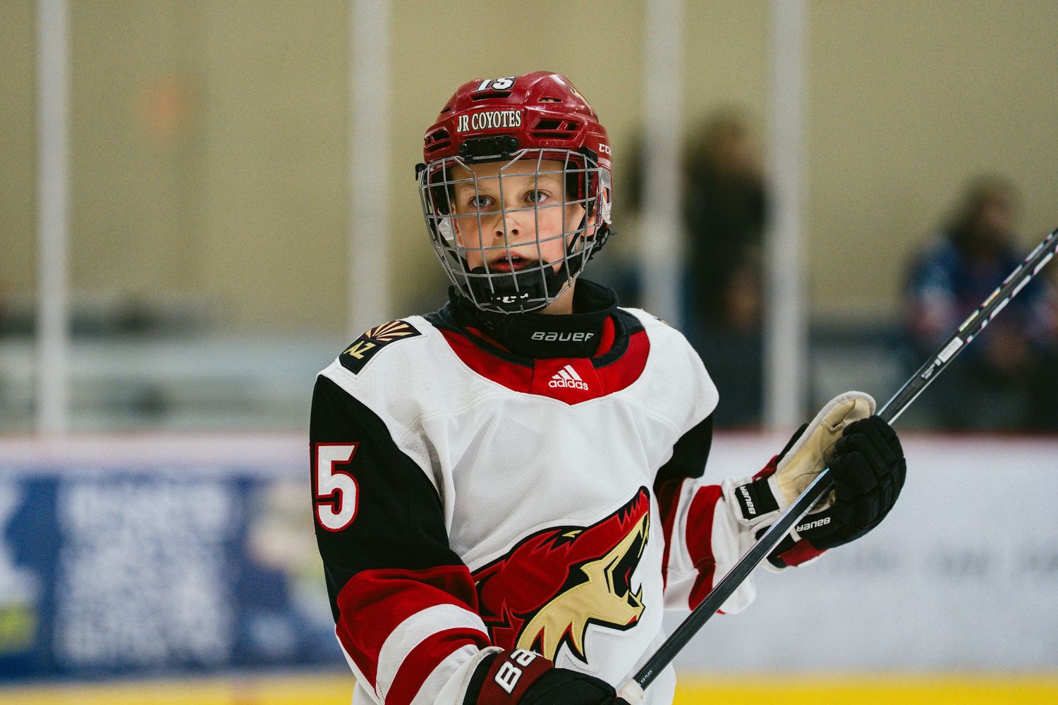 Youth hockey player in a red and white jersey holds a hockey stick during a game.