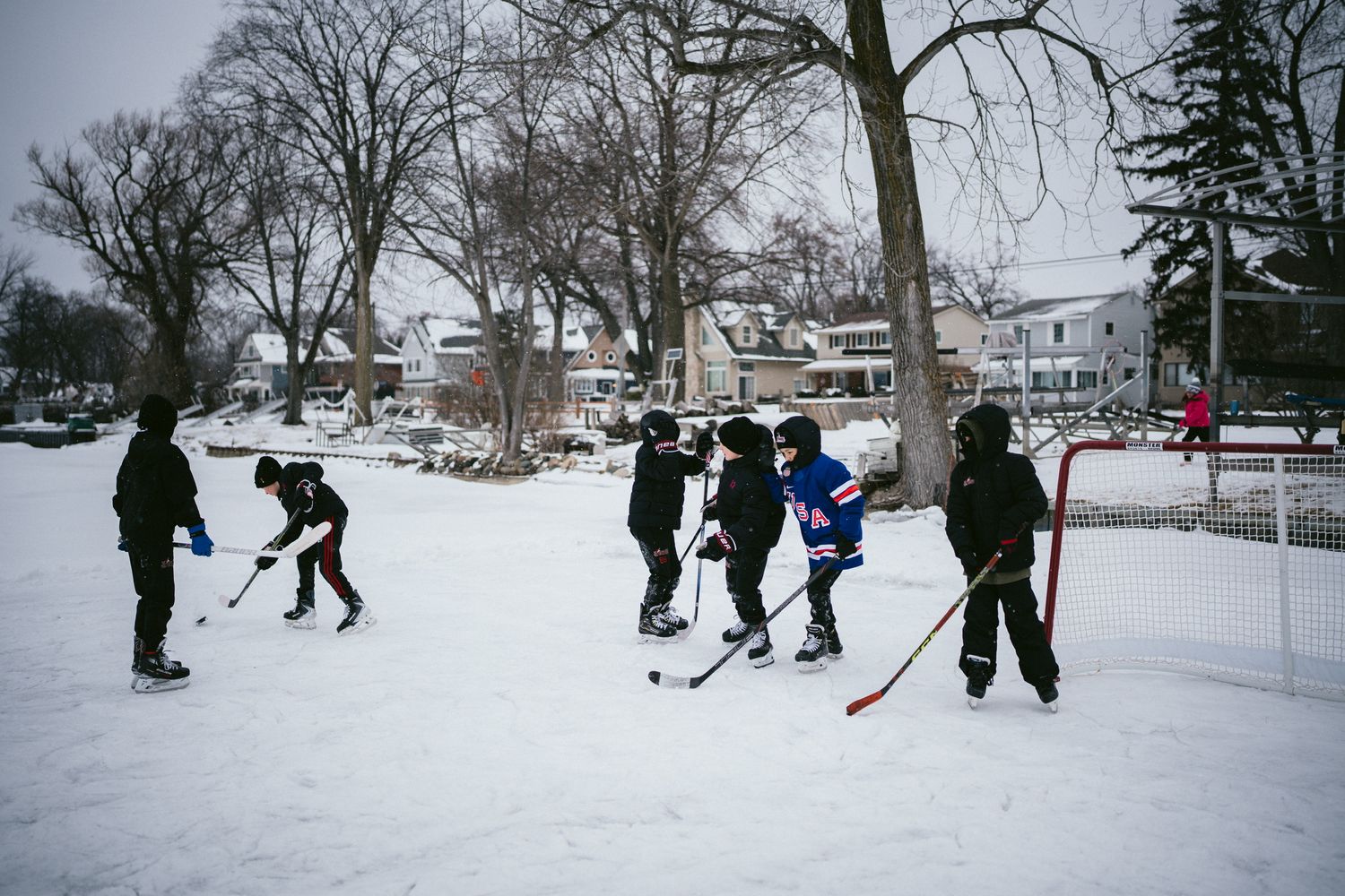 People playing hockey on a snowy outdoor rink surrounded by winter trees.