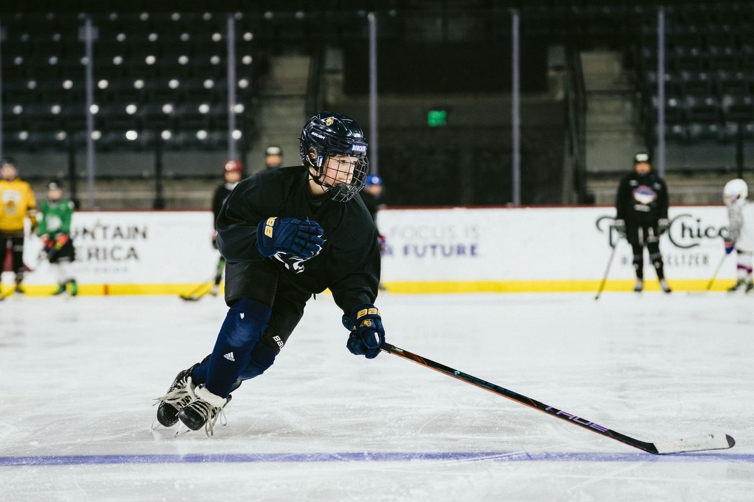Hockey player in black jersey skating aggressively with a stick during an indoor ice hockey practice session.