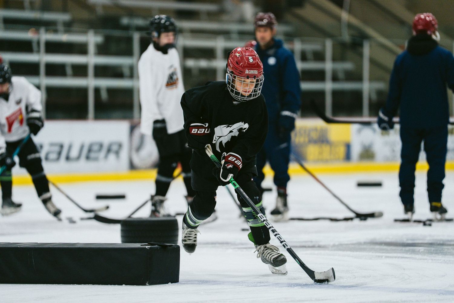 Youth hockey player in red helmet and black jersey skating with puck during ice practice.