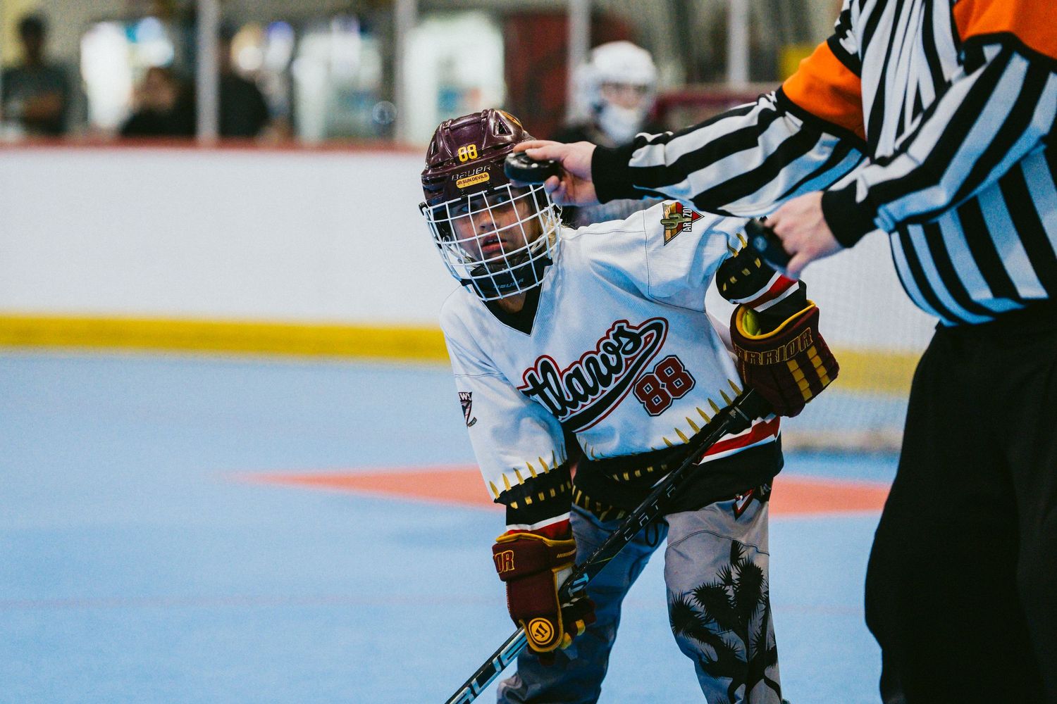 Young hockey player stands near a referee on an indoor rink during a youth hockey game.