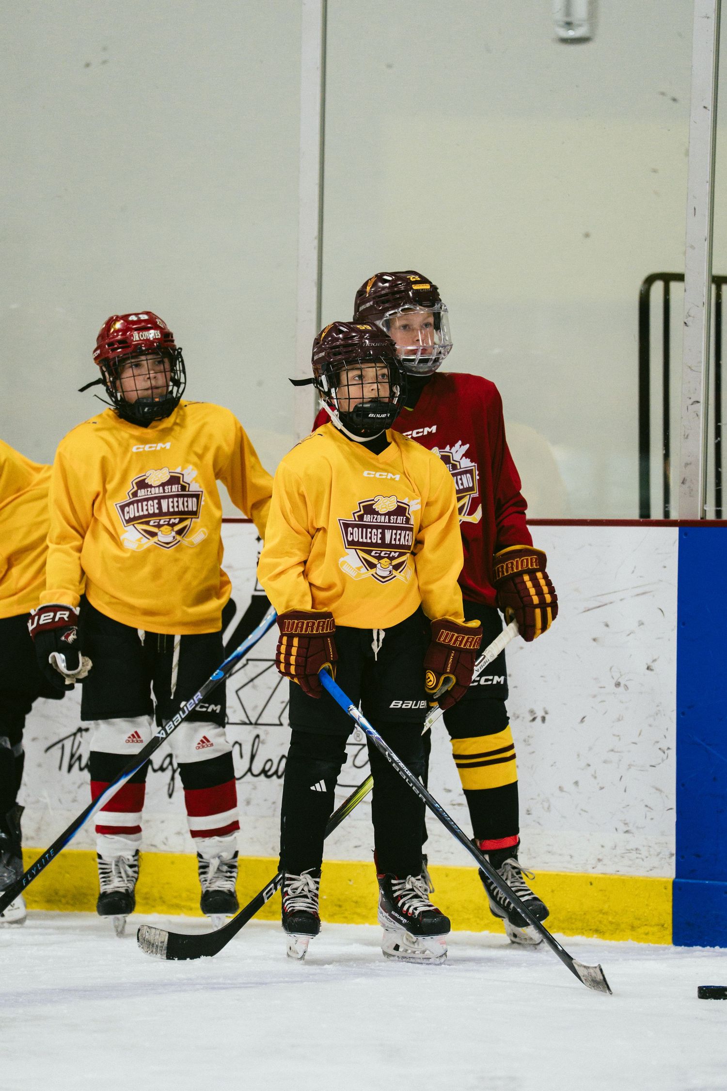 Young hockey players in yellow jerseys practice on indoor ice rink during a college weekend hockey camp.