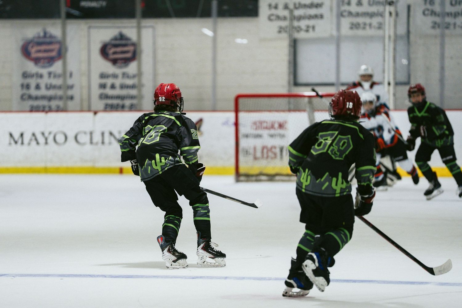 Youth hockey players in black green uniforms skating during competitive ice hockey game at arena.