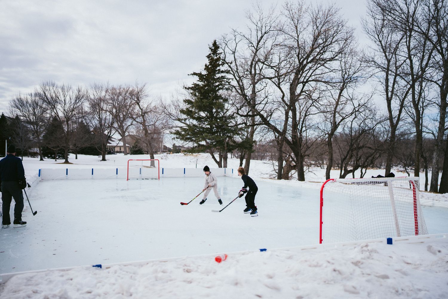 People playing hockey on an outdoor rink with red goal markers in the snow.