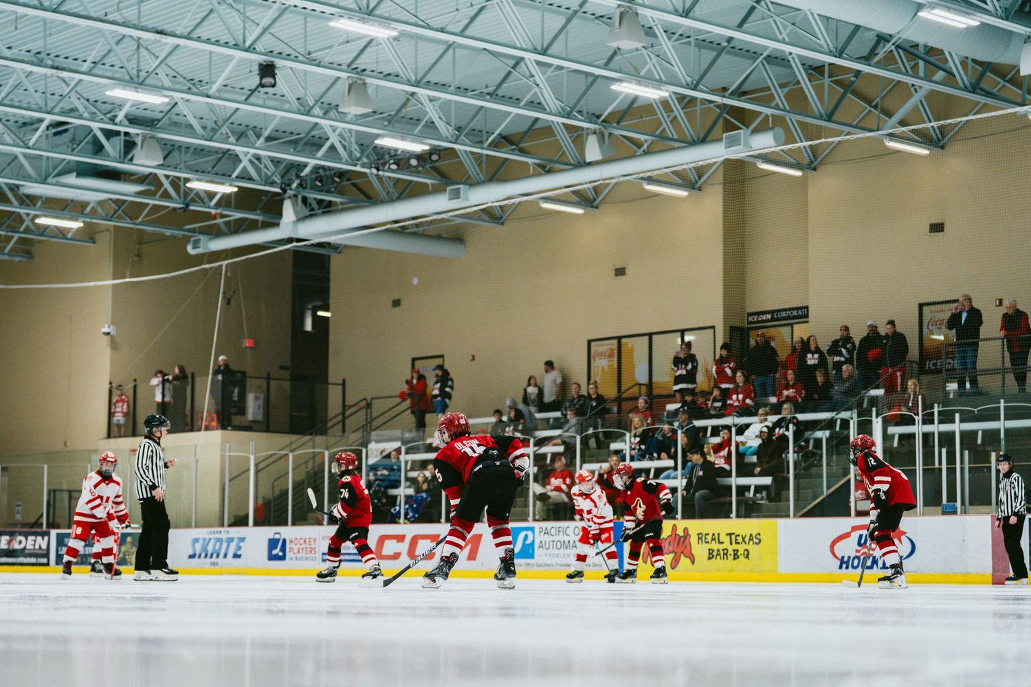 Wide panoramic view of an indoor ice hockey rink during a game with players in red and white jerseys on the ice.