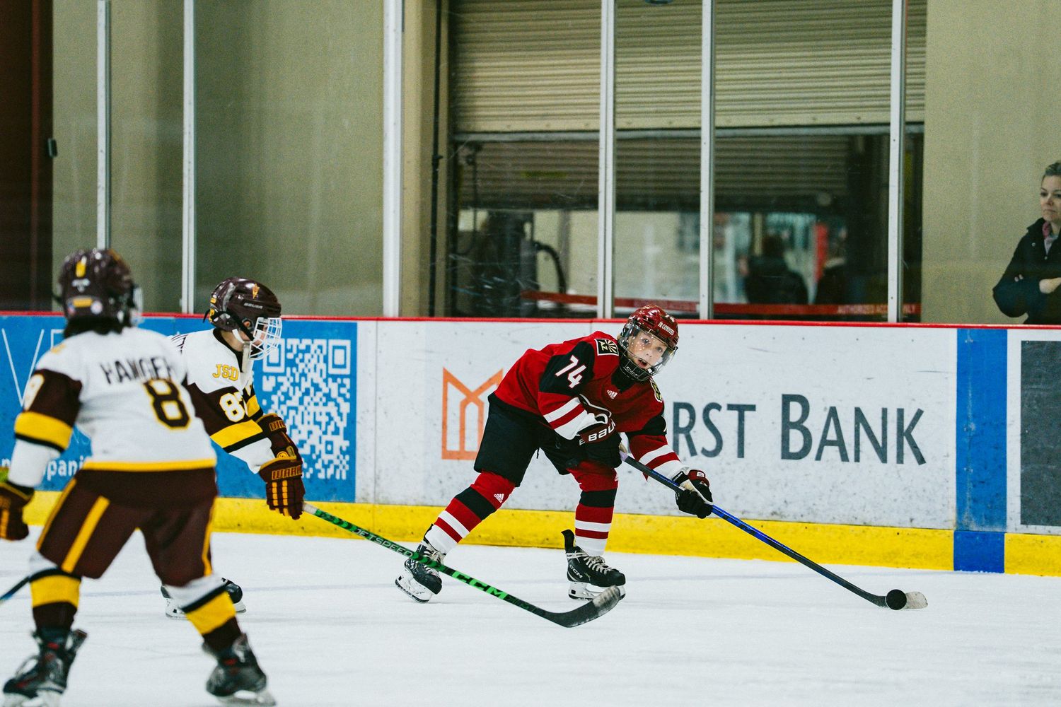 Ice hockey players in yellow and red jerseys compete during a game with arena advertisements visible.