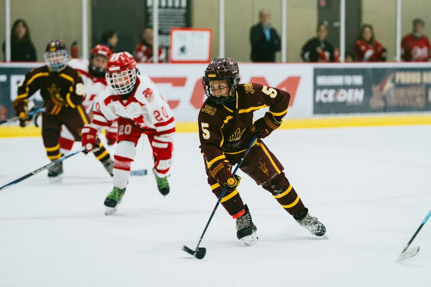 Youth hockey players chase the puck during a competitive game on indoor ice rink.