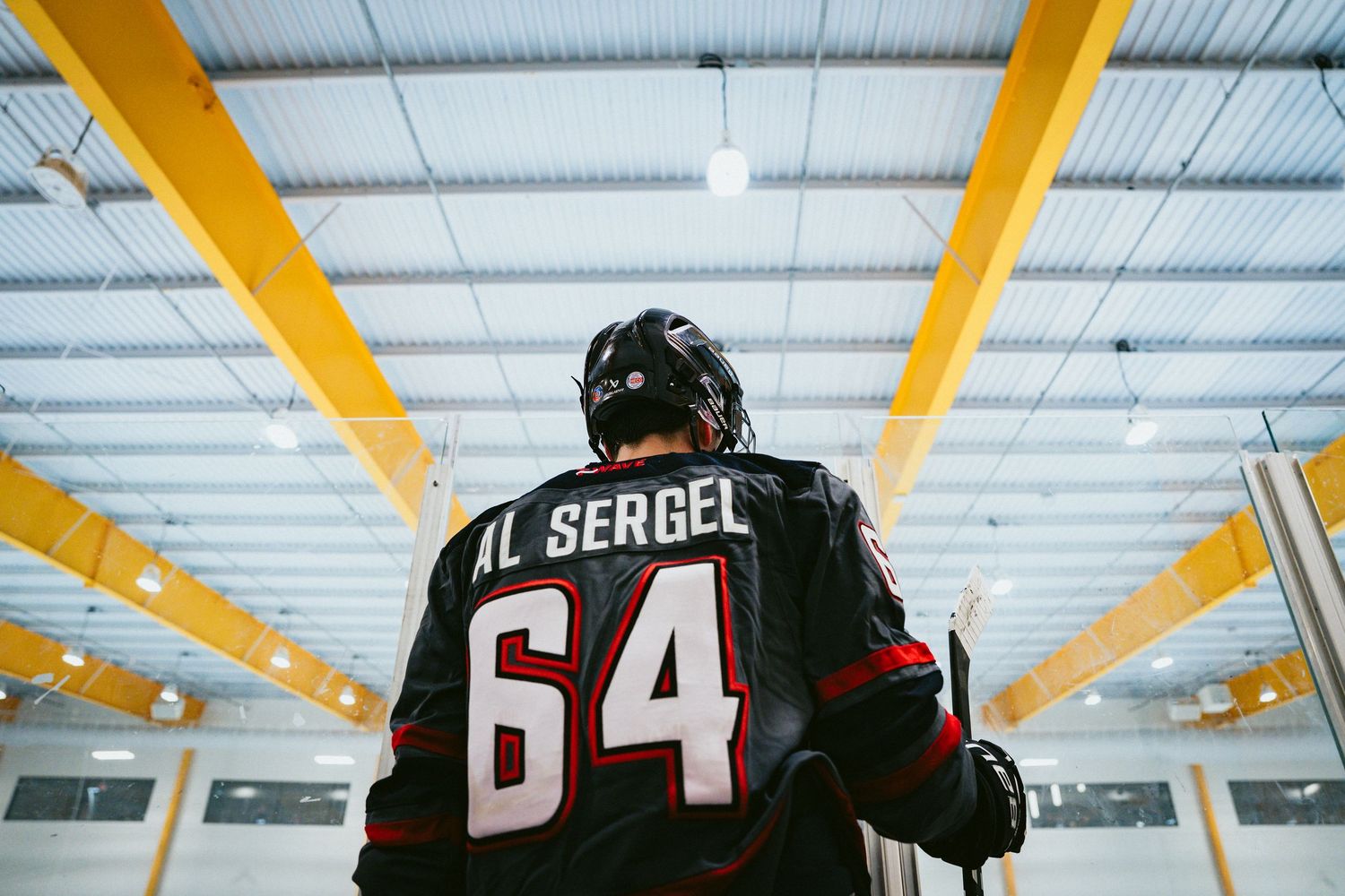 A hockey player wearing jersey number 64 with the name Al Sergel stands in an indoor arena.