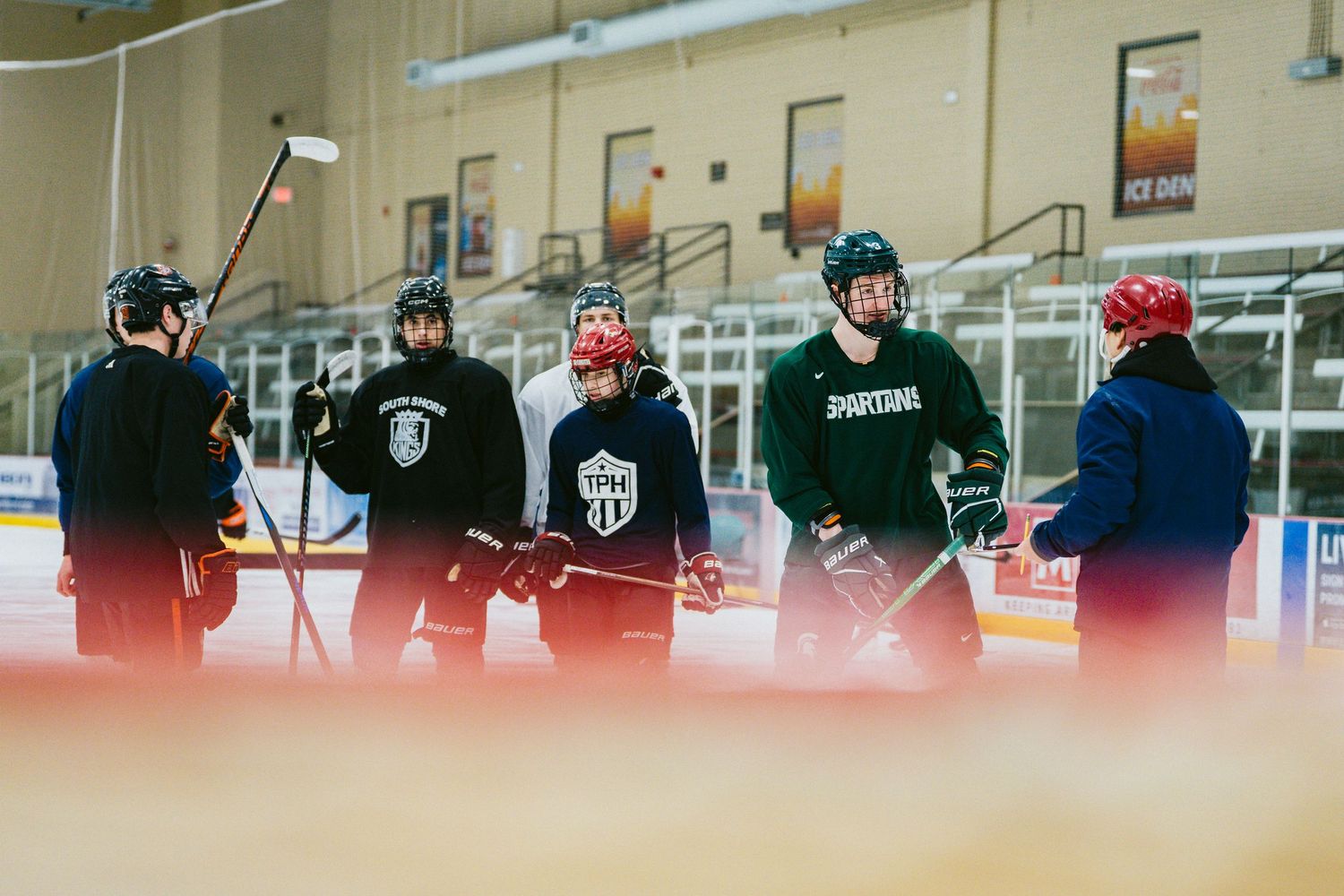 Group of hockey players in TPH jerseys gather on ice rink during team practice session.