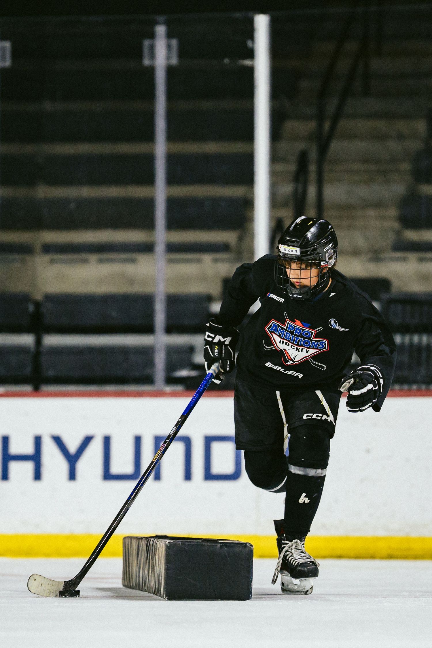 Youth hockey player practices puck handling drill with training block on ice at Hyundai-sponsored arena.